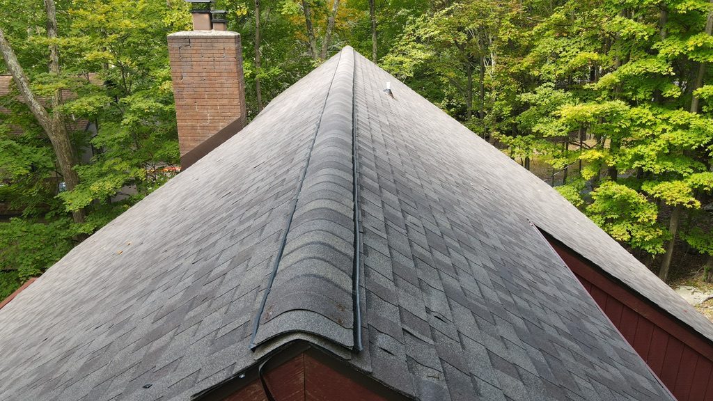 Close-up of a freshly installed shingle roof ridge line with a brick chimney